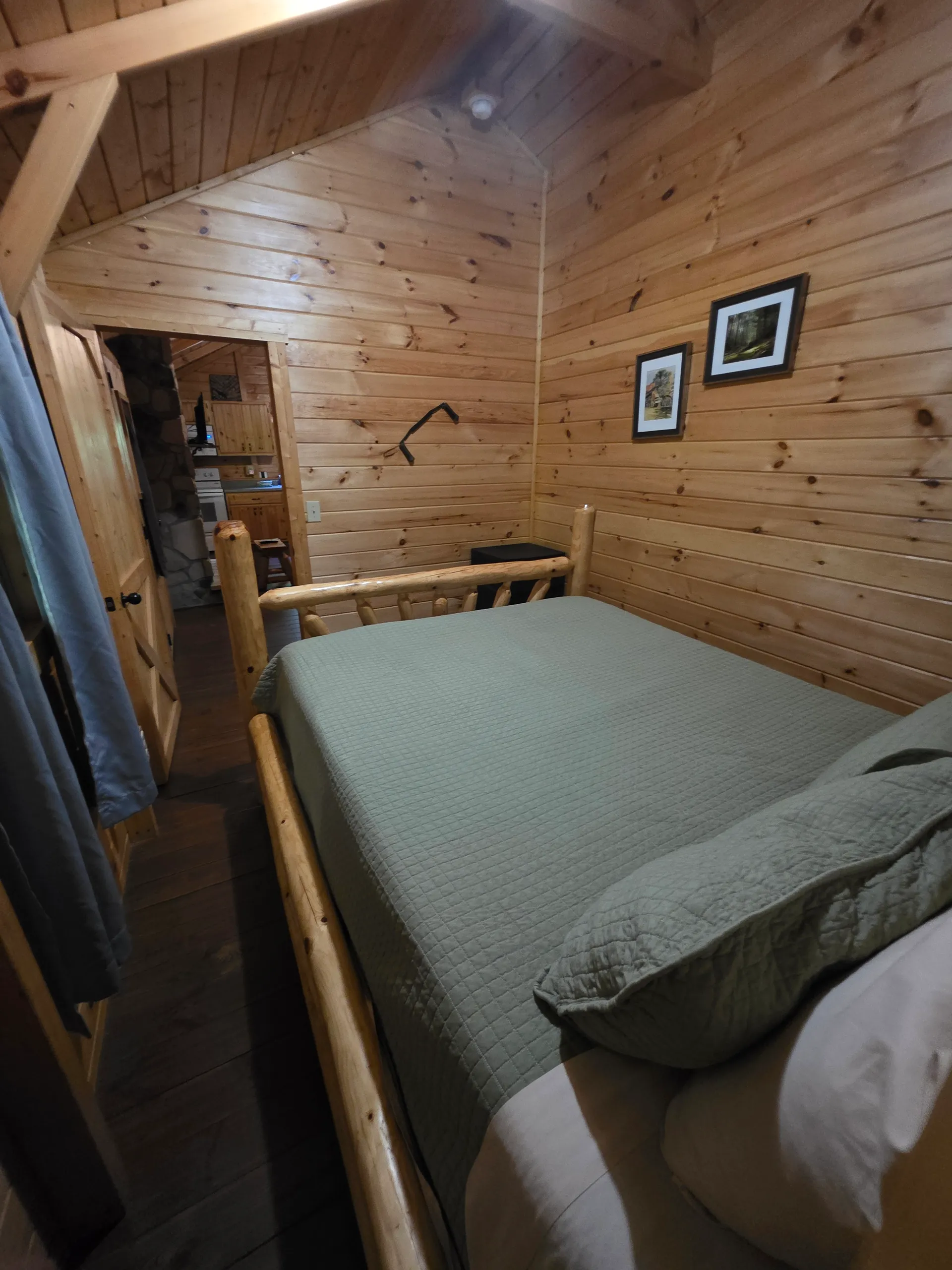 Loft bedroom with log bed frame and green bedding inside Millers Den cabin