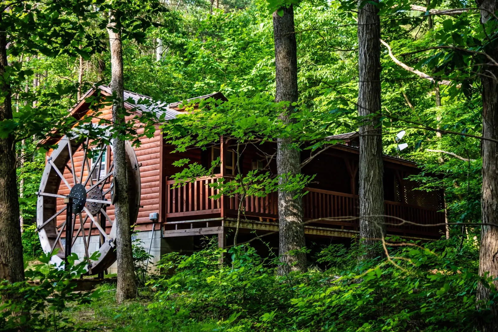 Full exterior view of Millers Den cabin with water wheel nestled among Hocking Hills trees