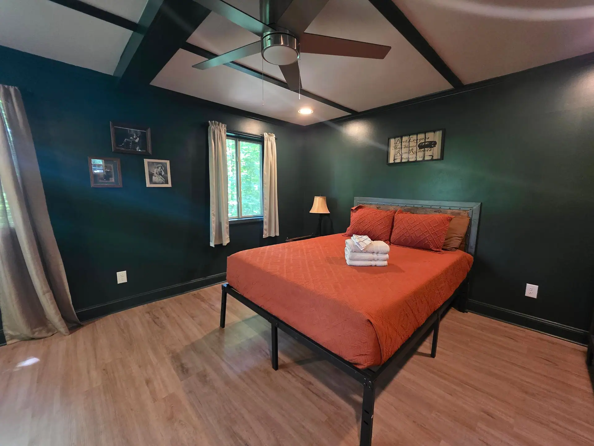 Bedroom with queen bed, rust bedspread, ceiling fan and dark green walls at The Old Moonshiner cabin