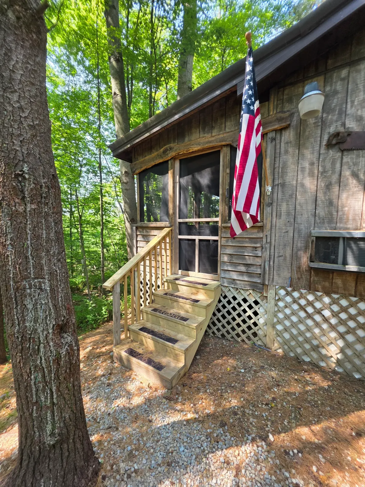 Wooden porch and stairs with American flag at the entrance to Moonshiner cabin in the forest