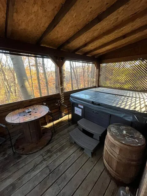 Hot tub on covered deck with spool table and whiskey barrel amid fall foliage at Moonshiner cabin