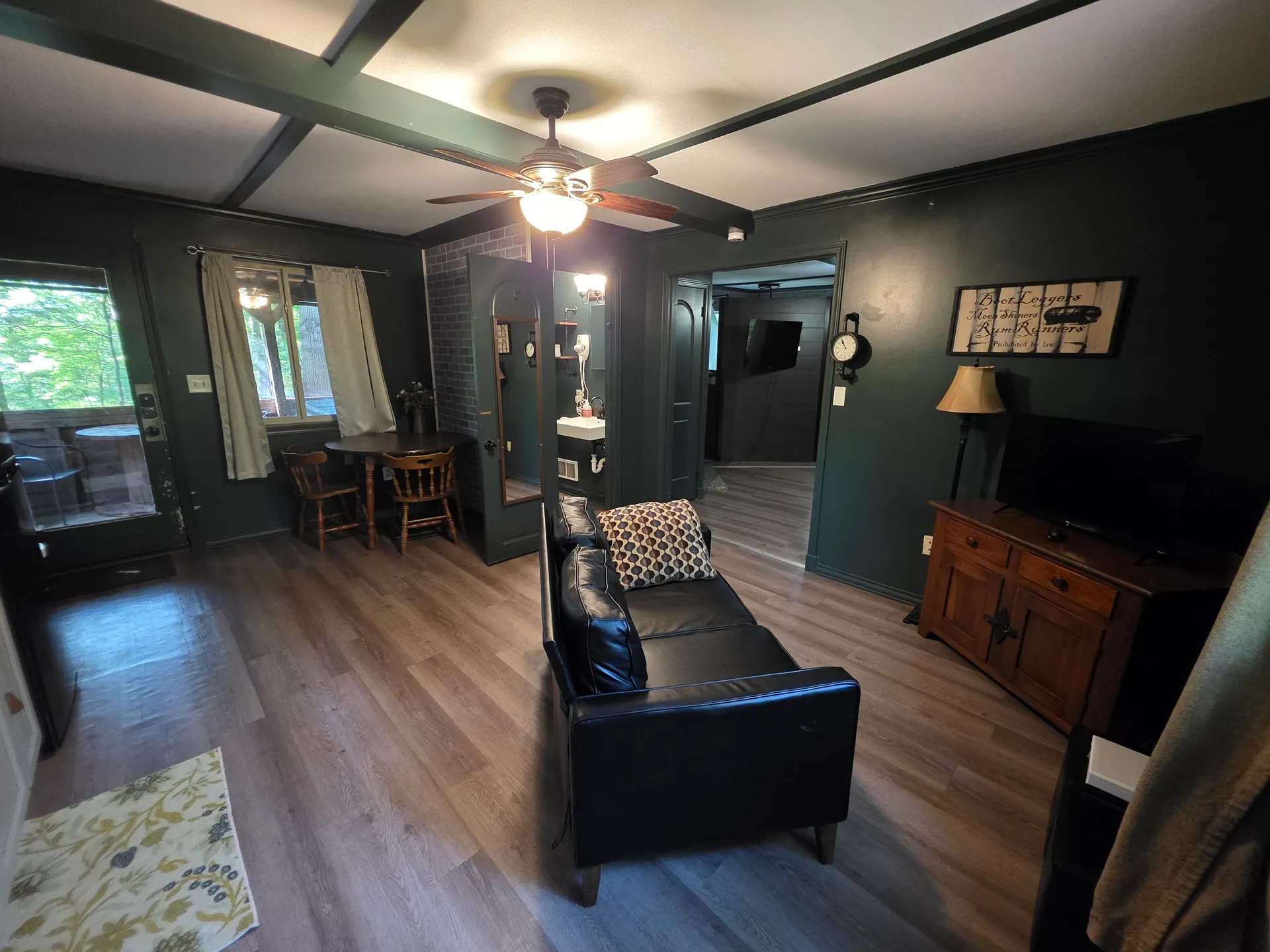 Dark green living room with black leather sofa, ceiling fan, and moonshine-themed decor at Moonshiner cabin