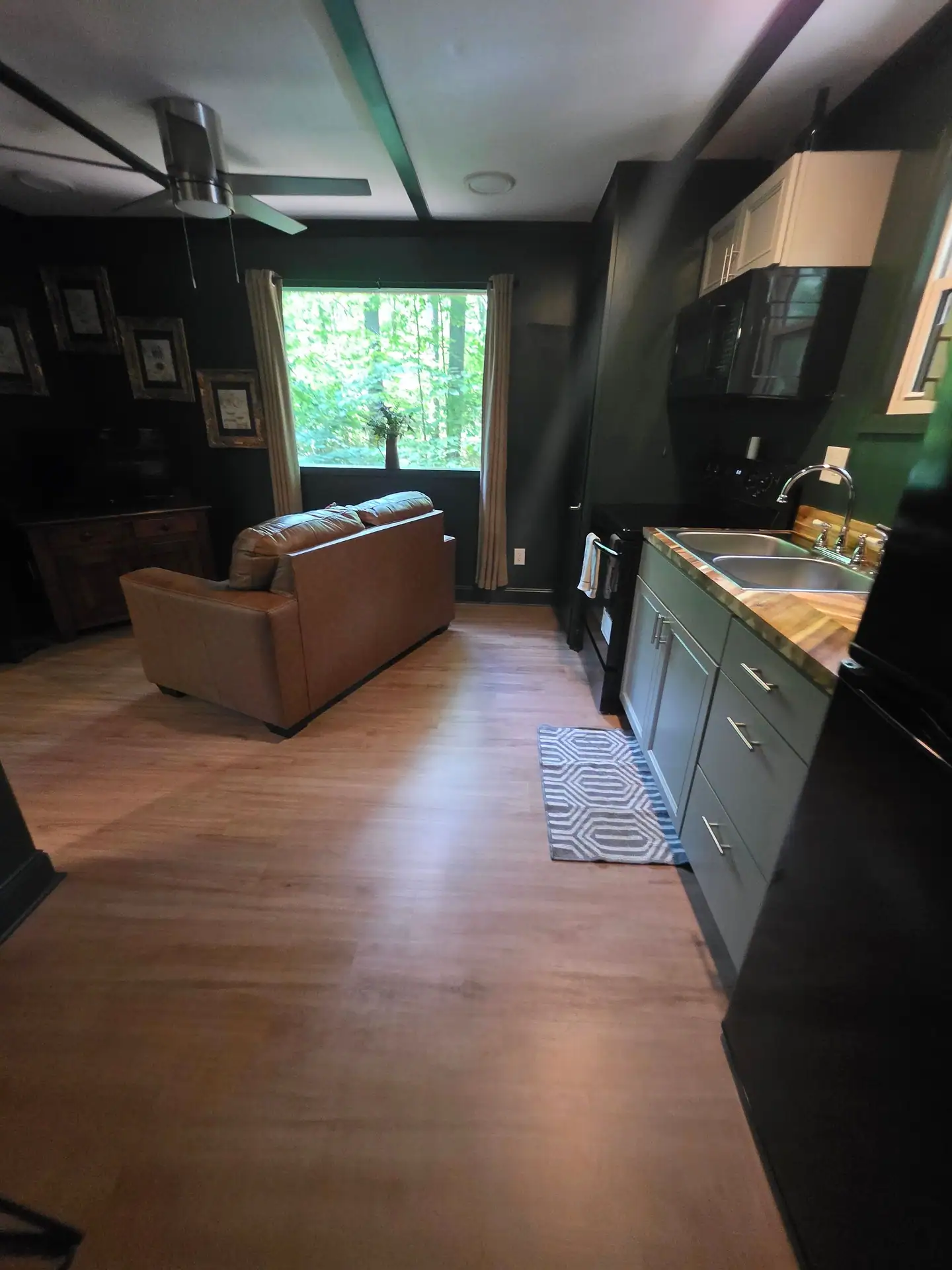 Open living area with dark green walls, leather loveseat and kitchen along the wall at The Old Moonshiner cabin