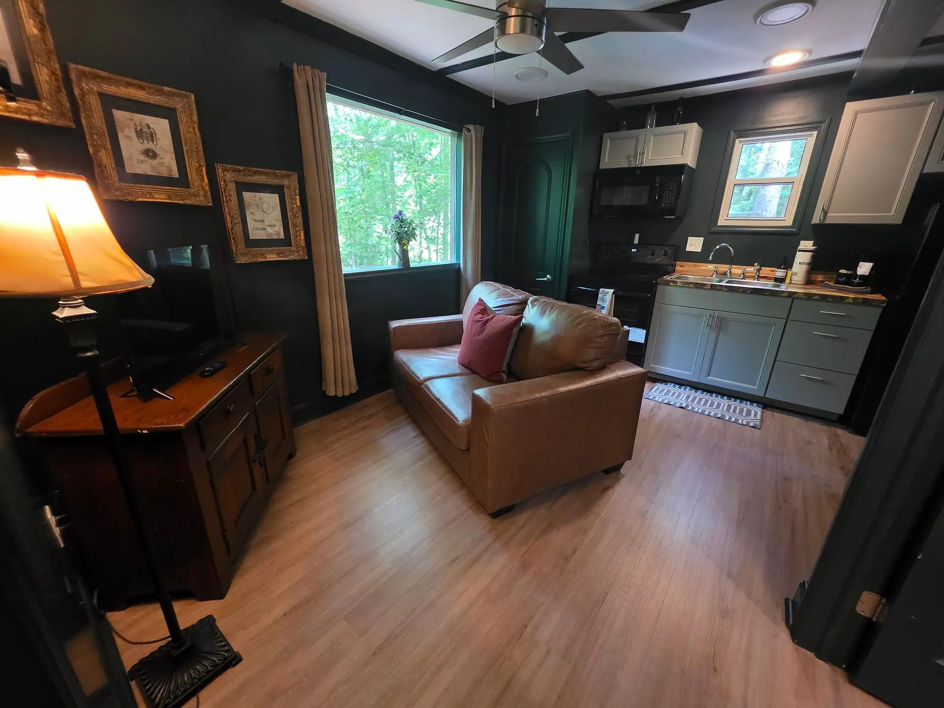 Living room with leather loveseat, TV cabinet and view into the kitchen at The Old Moonshiner cabin