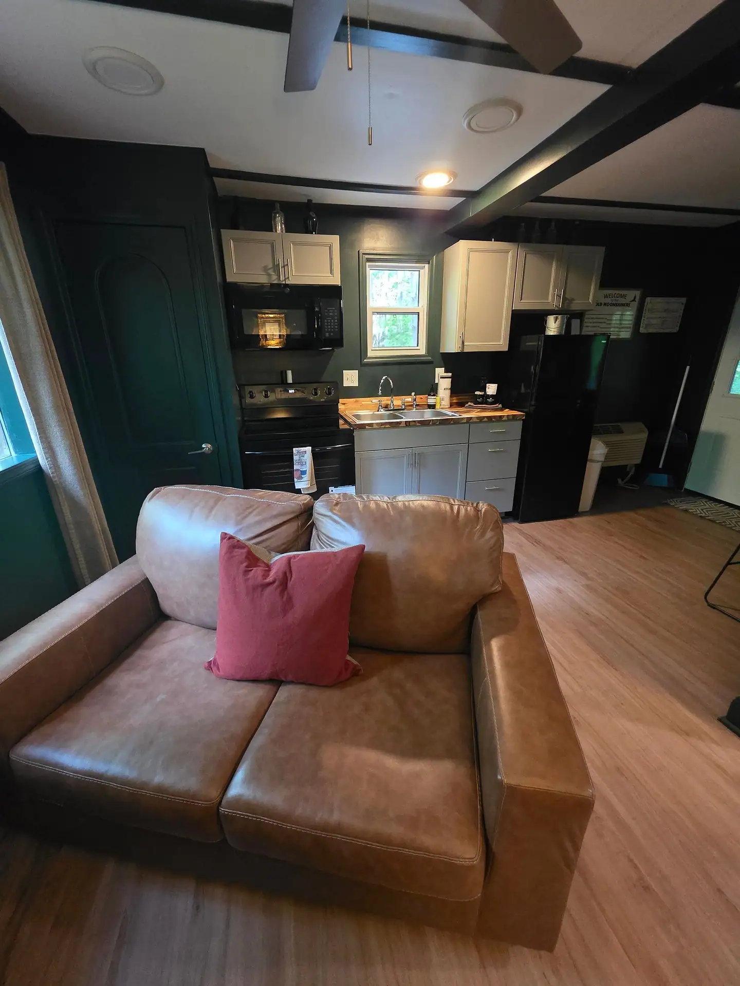 Leather loveseat with a red pillow facing the kitchen at The Old Moonshiner cabin