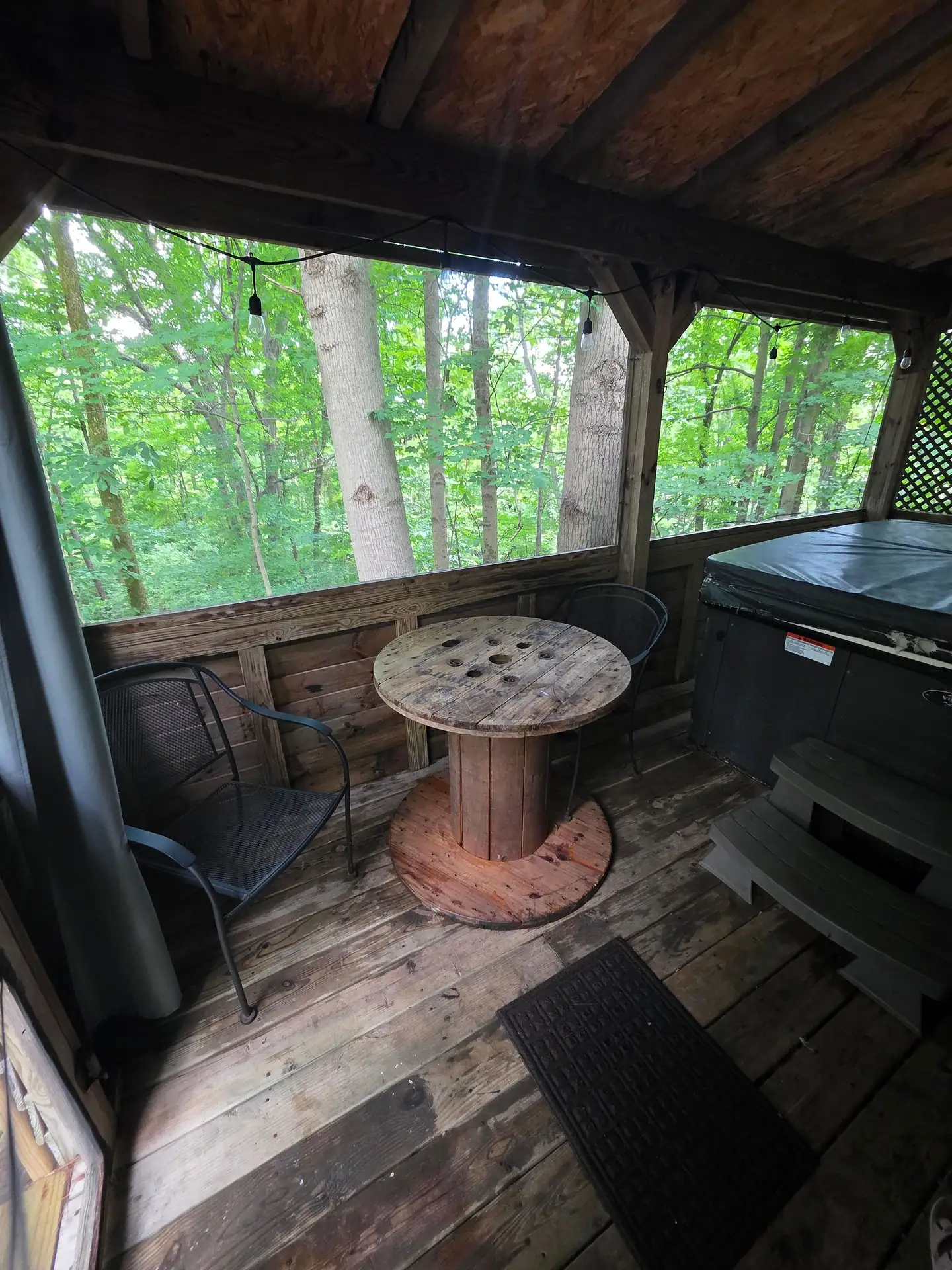 Screened porch with spool table, chairs and forest view beside the hot tub at The Old Moonshiner cabin