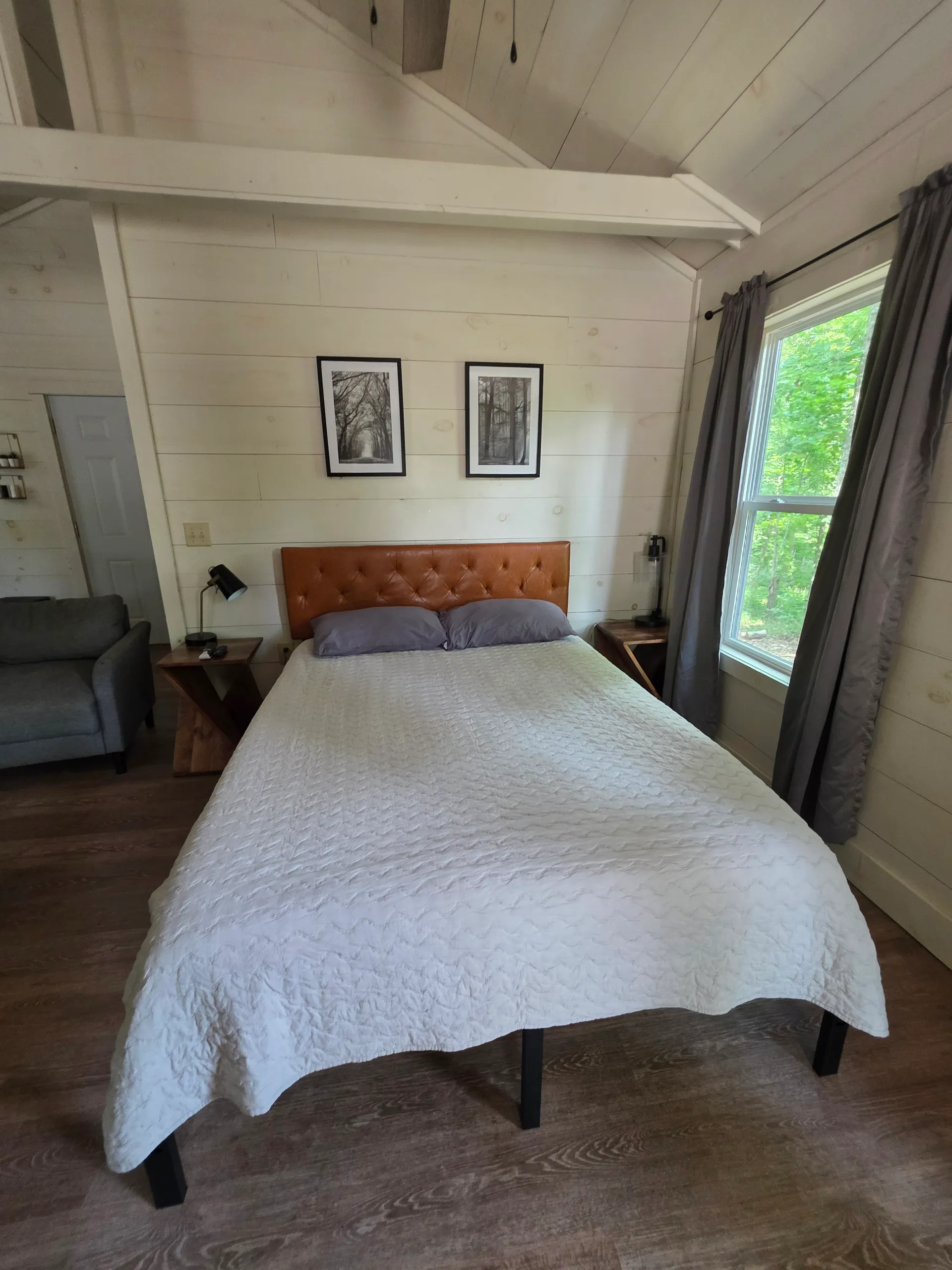 Queen bed with white linens, tufted caramel headboard, and framed nature prints at Owl's Tale cabin