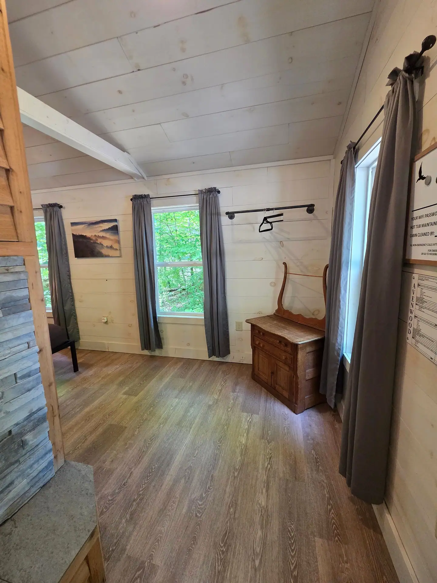 Bedroom corner with wooden dresser, clothing rack, and two windows at Owl's Tale cabin