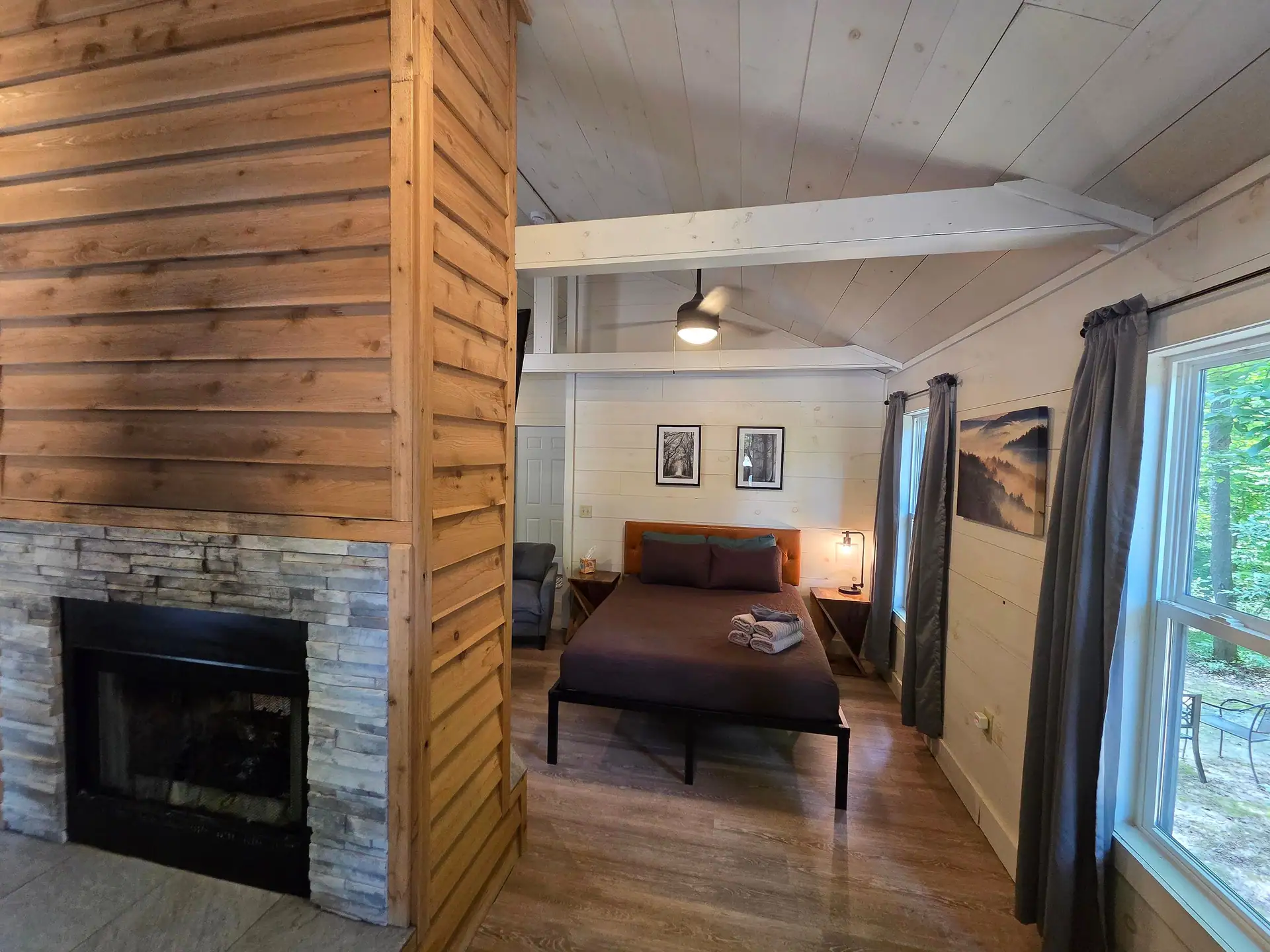 Queen bed seen past the bedroom side of the double-sided fireplace at Owl's Tale cabin