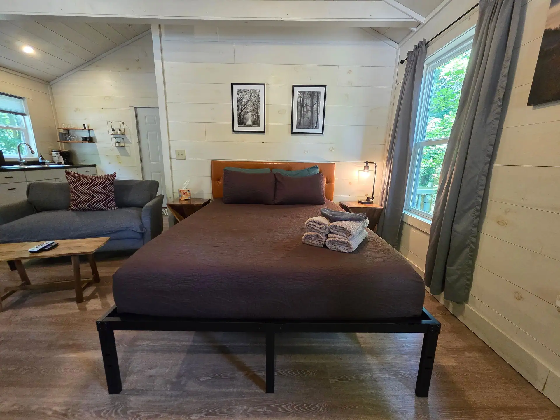 Queen bed with brown linens and framed nature prints beside a window at Owl's Tale cabin