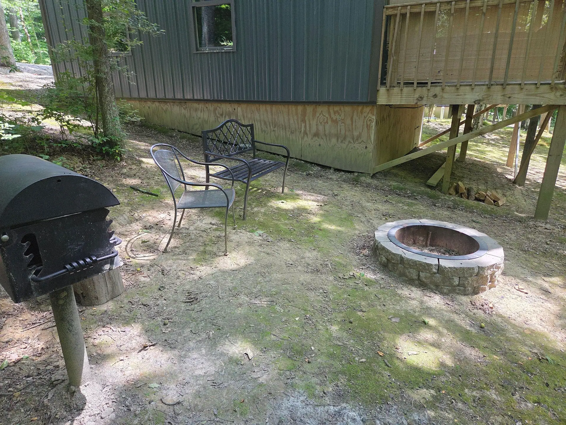Charcoal grill with patio chairs and fire pit below the deck at Owl's Tale cabin