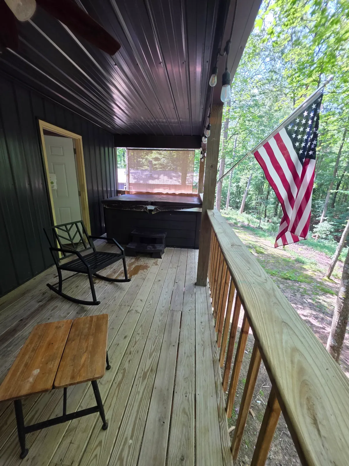 Back deck with American flag, bistro table, and hot tub at Owl's Tale cabin