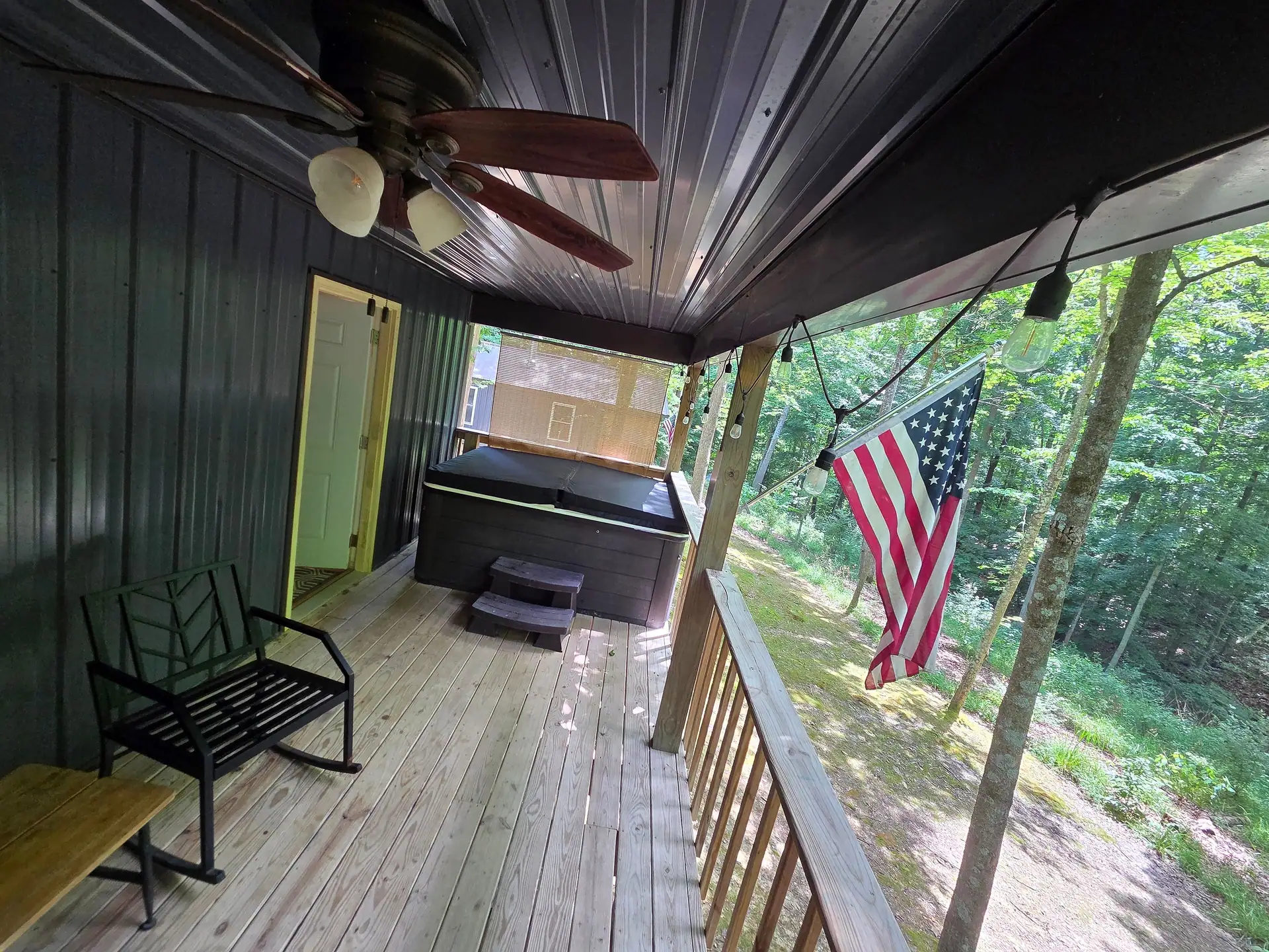 Covered back deck with private hot tub, rocking chair, and American flag at Owl's Tale cabin