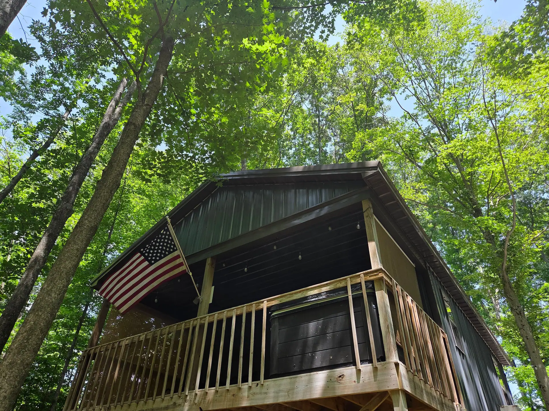 Covered back deck with American flag seen from below among tall trees at Owl's Tale cabin