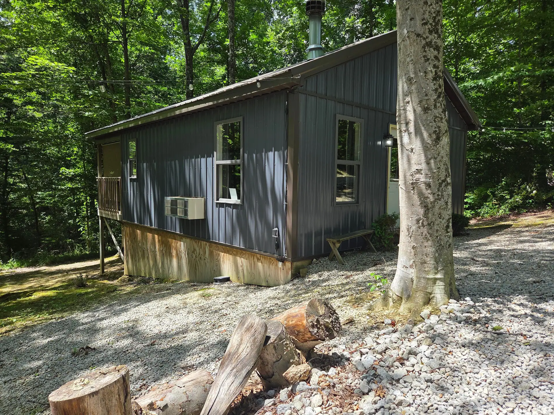 Side view of the dark gray cabin with tree-stump and log accents on the gravel at Owl's Tale cabin