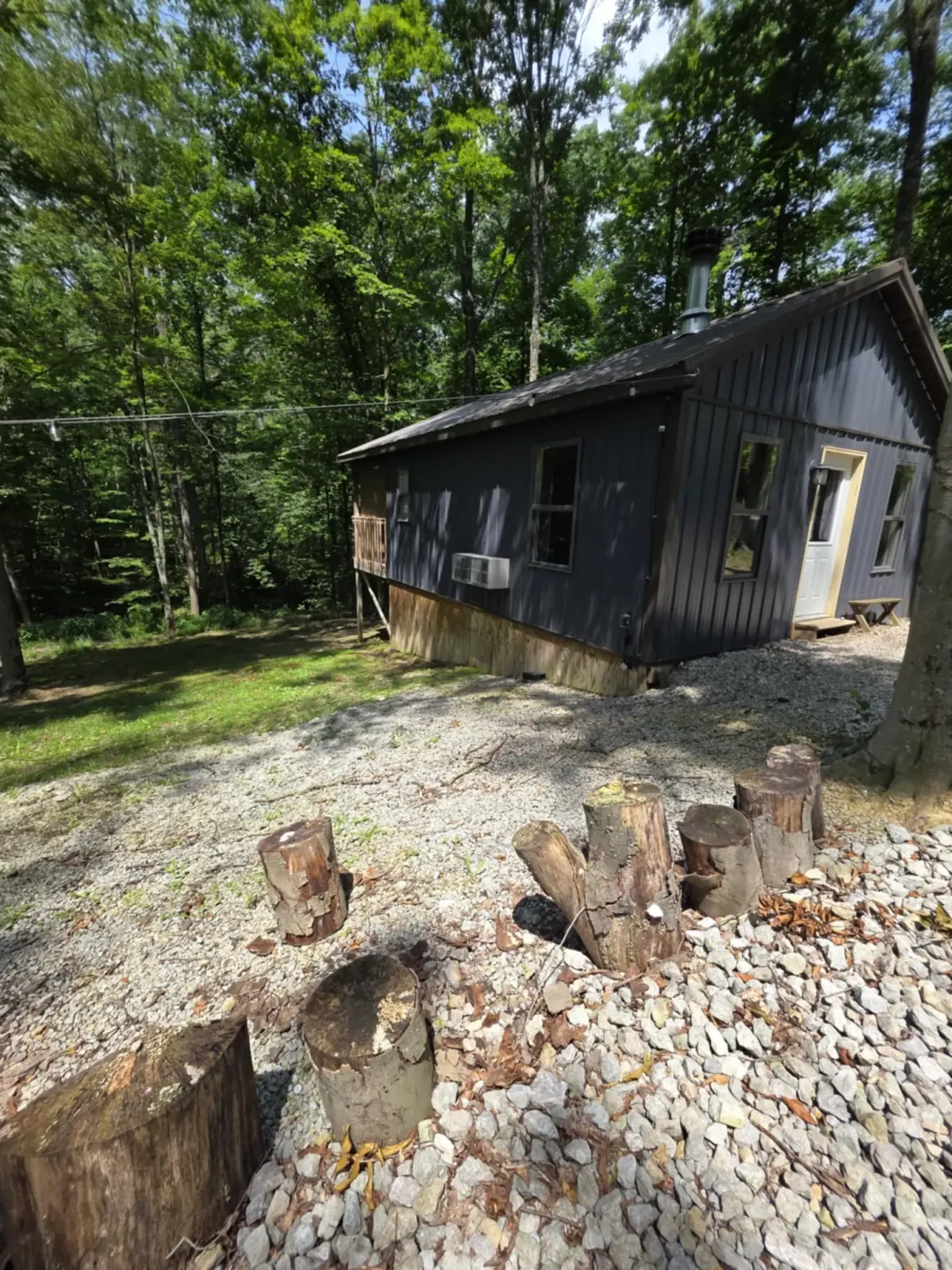 Side view of Owl's Tale cabin with decorative log stumps and gravel path
