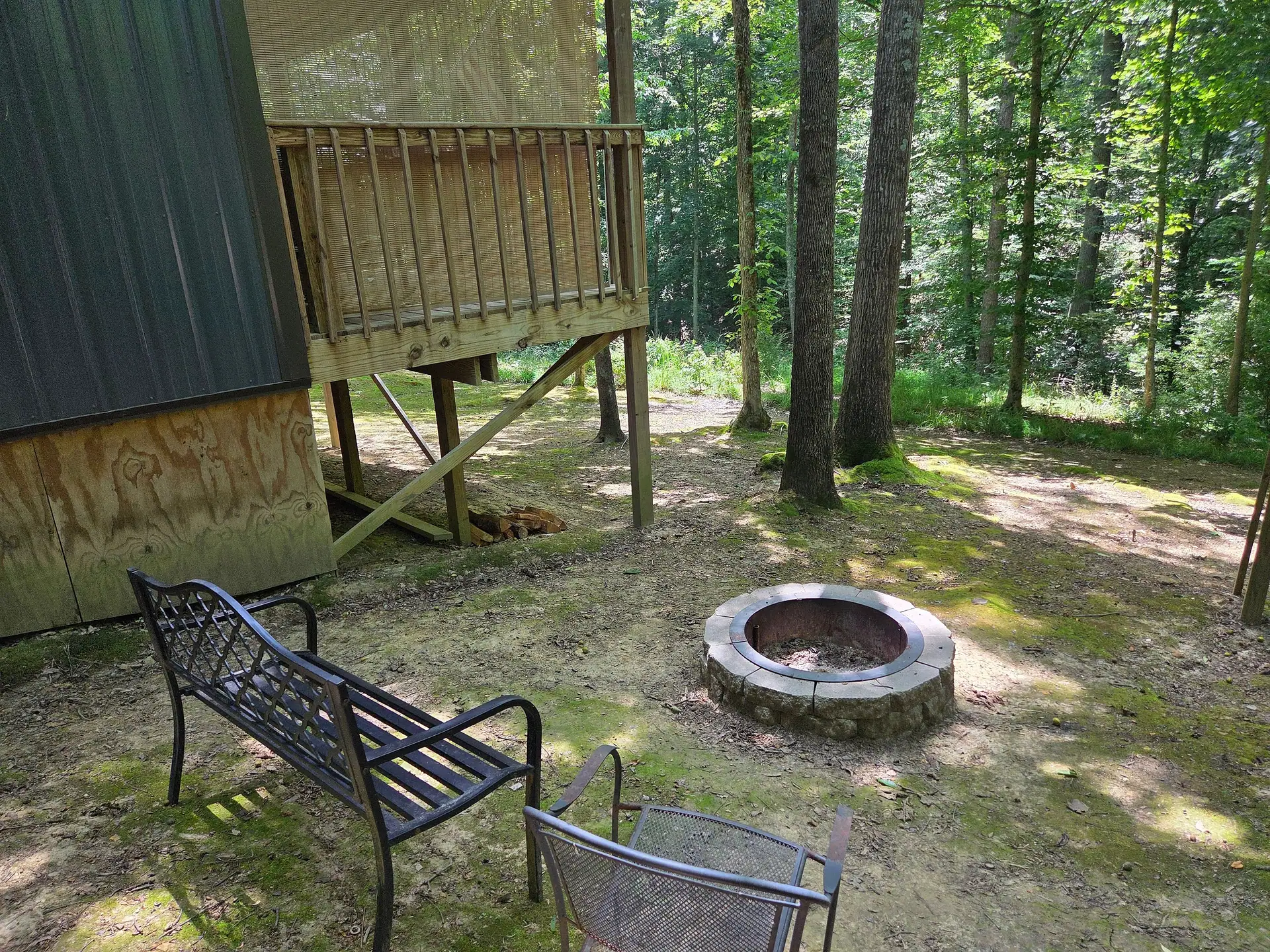 Stone fire pit with metal bench and chair under the trees at Owl's Tale cabin