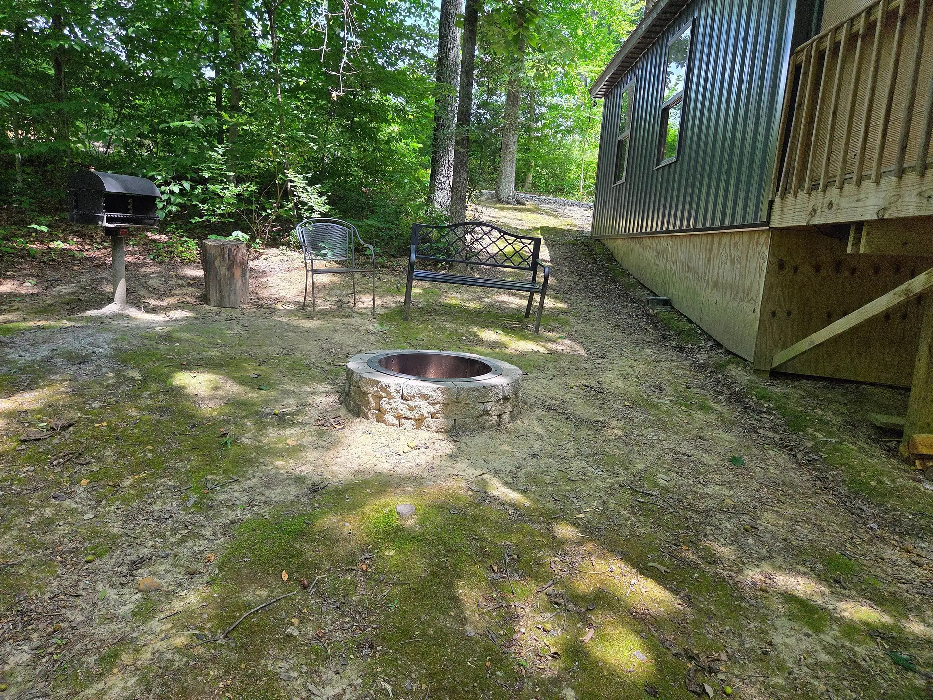 Stone fire pit with metal bench, chairs, and charcoal grill in the yard at Owl's Tale cabin