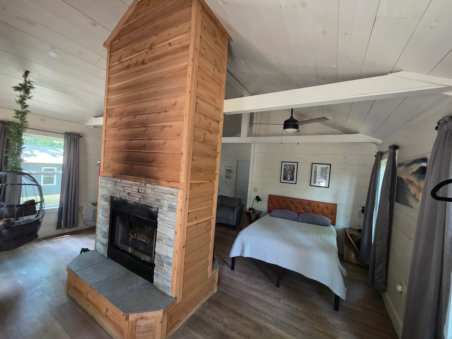 Bedroom side of the double-sided cedar fireplace with queen bed and hanging chair at Owl's Tale cabin