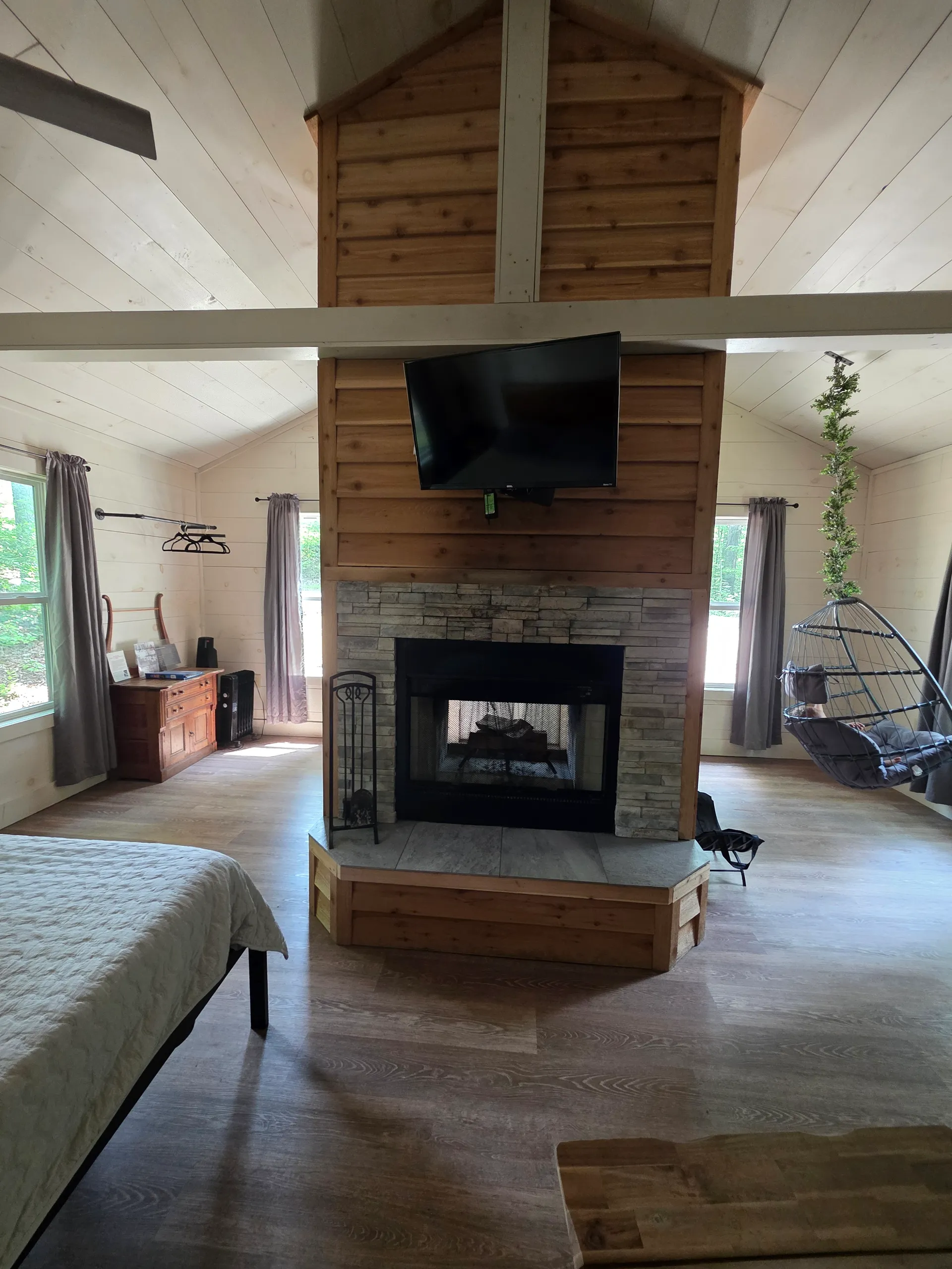 Double-sided cedar and stone fireplace with TV and hanging chair visible at Owl's Tale cabin