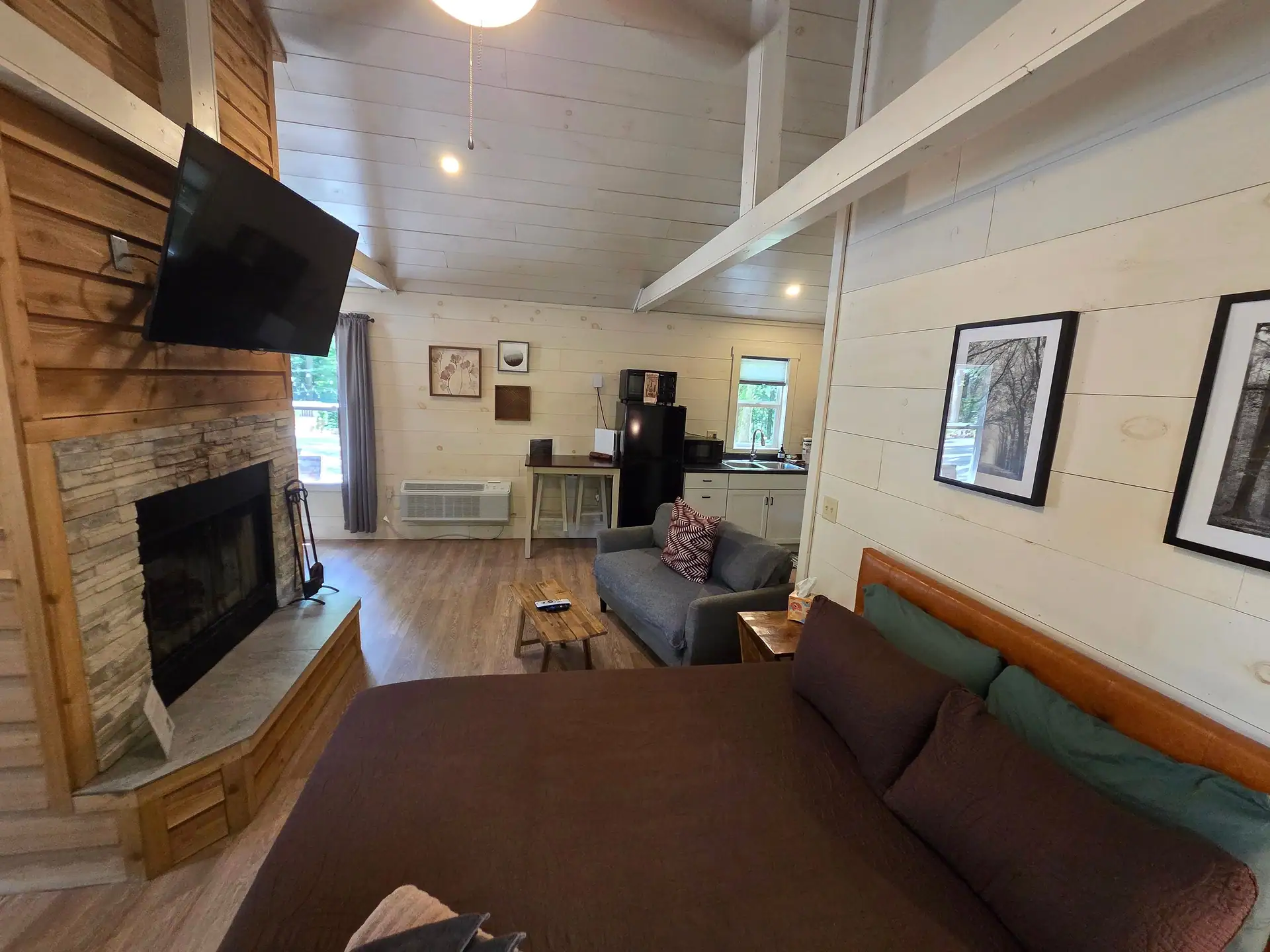 Double-sided cedar and stone fireplace with wall-mounted TV seen from the bed at Owl's Tale cabin