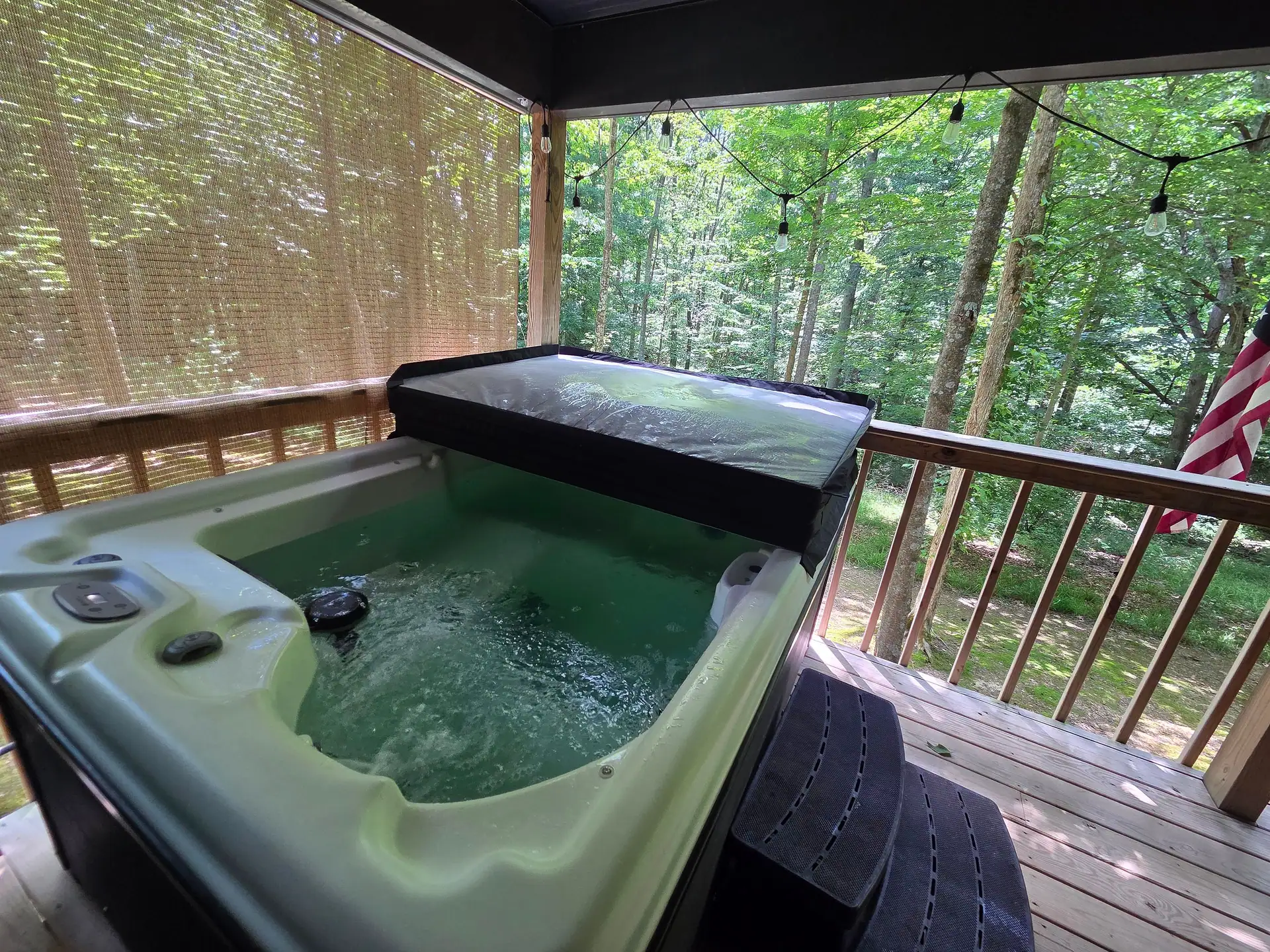 Private hot tub with the cover open on the covered back deck at Owl's Tale cabin