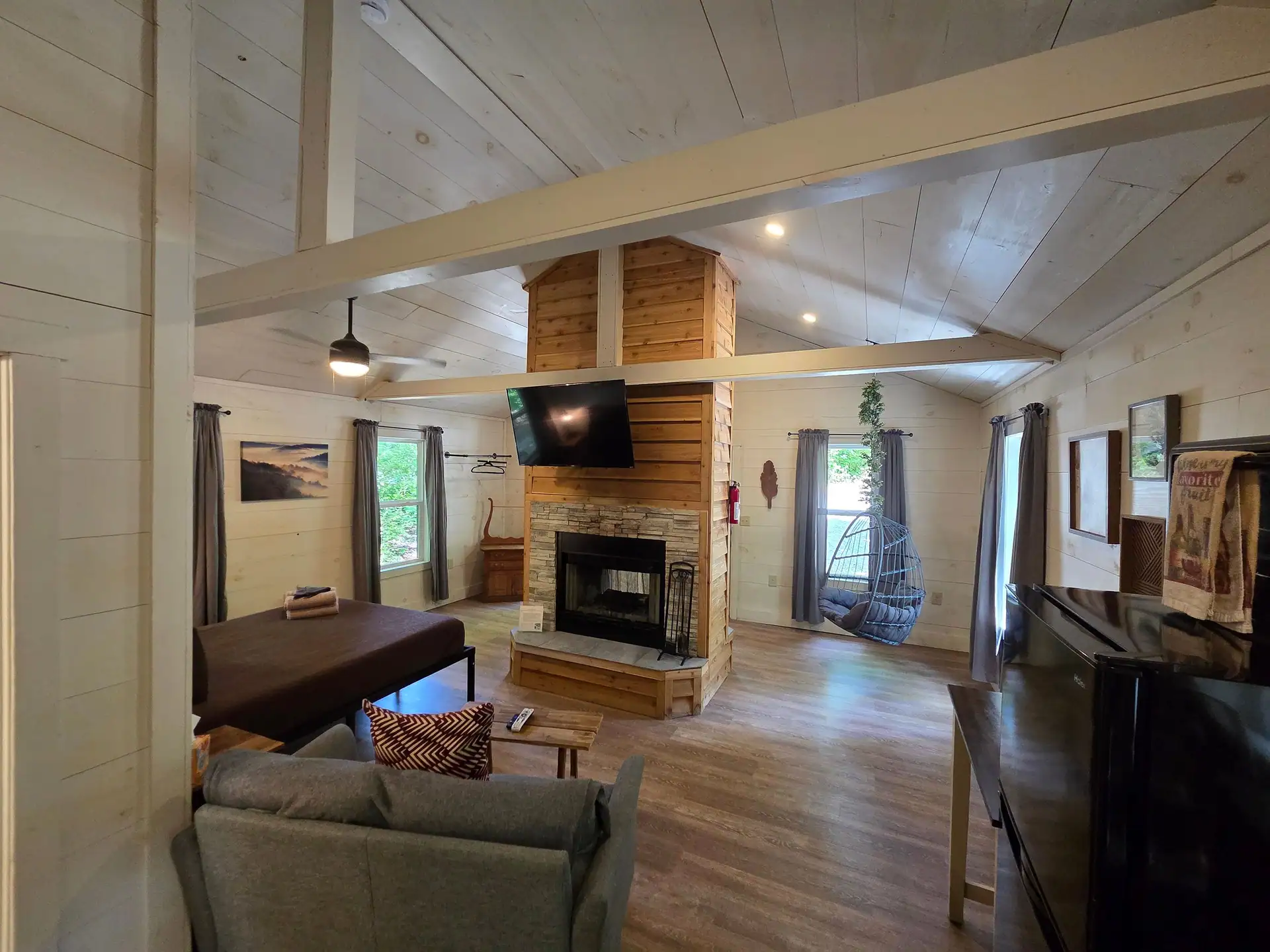 Open living area with sofa, TV, double-sided fireplace, and hanging chair at Owl's Tale cabin