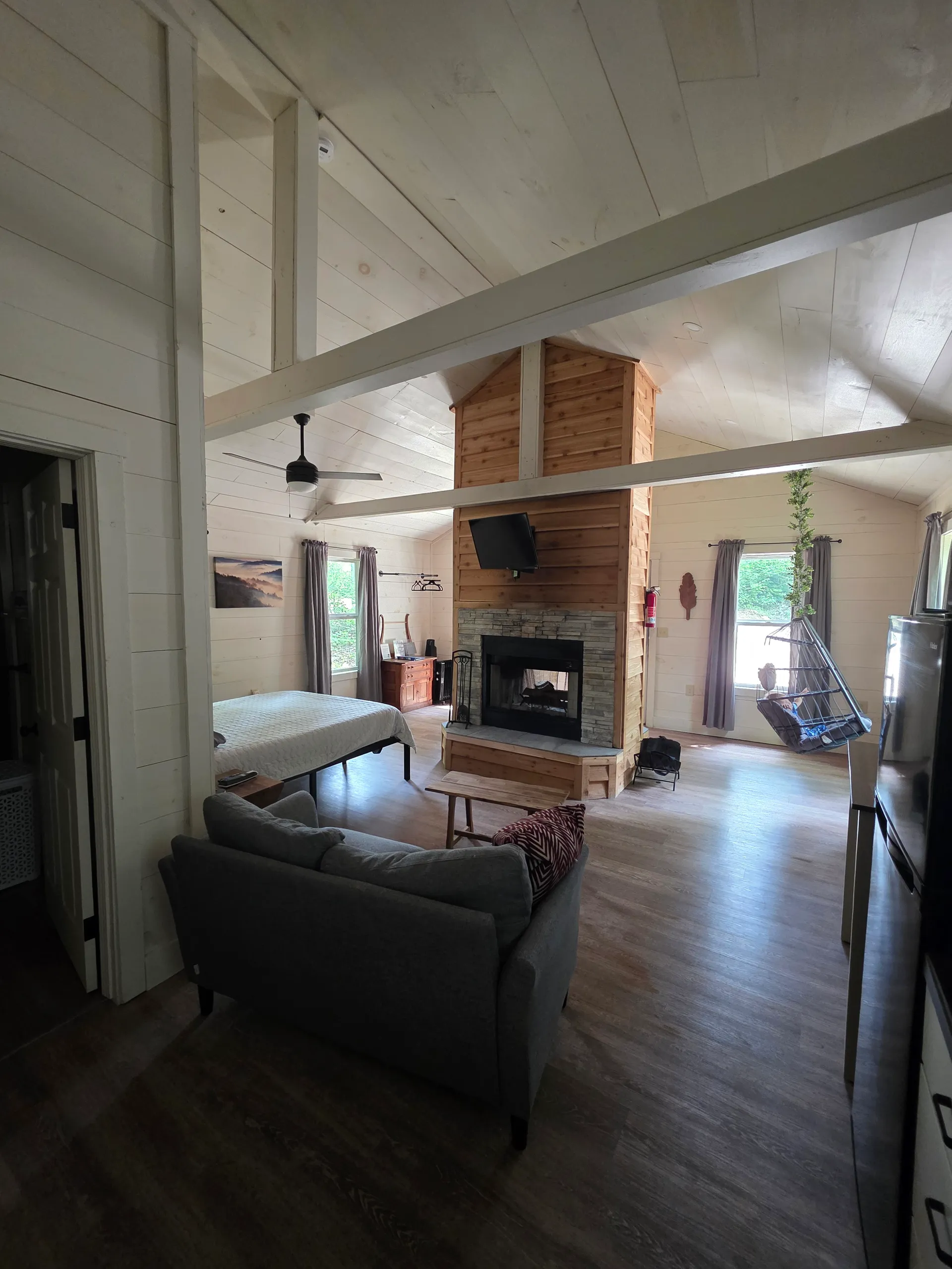 Open-concept interior with double-sided cedar fireplace, sofa, and bedroom at Owl's Tale cabin