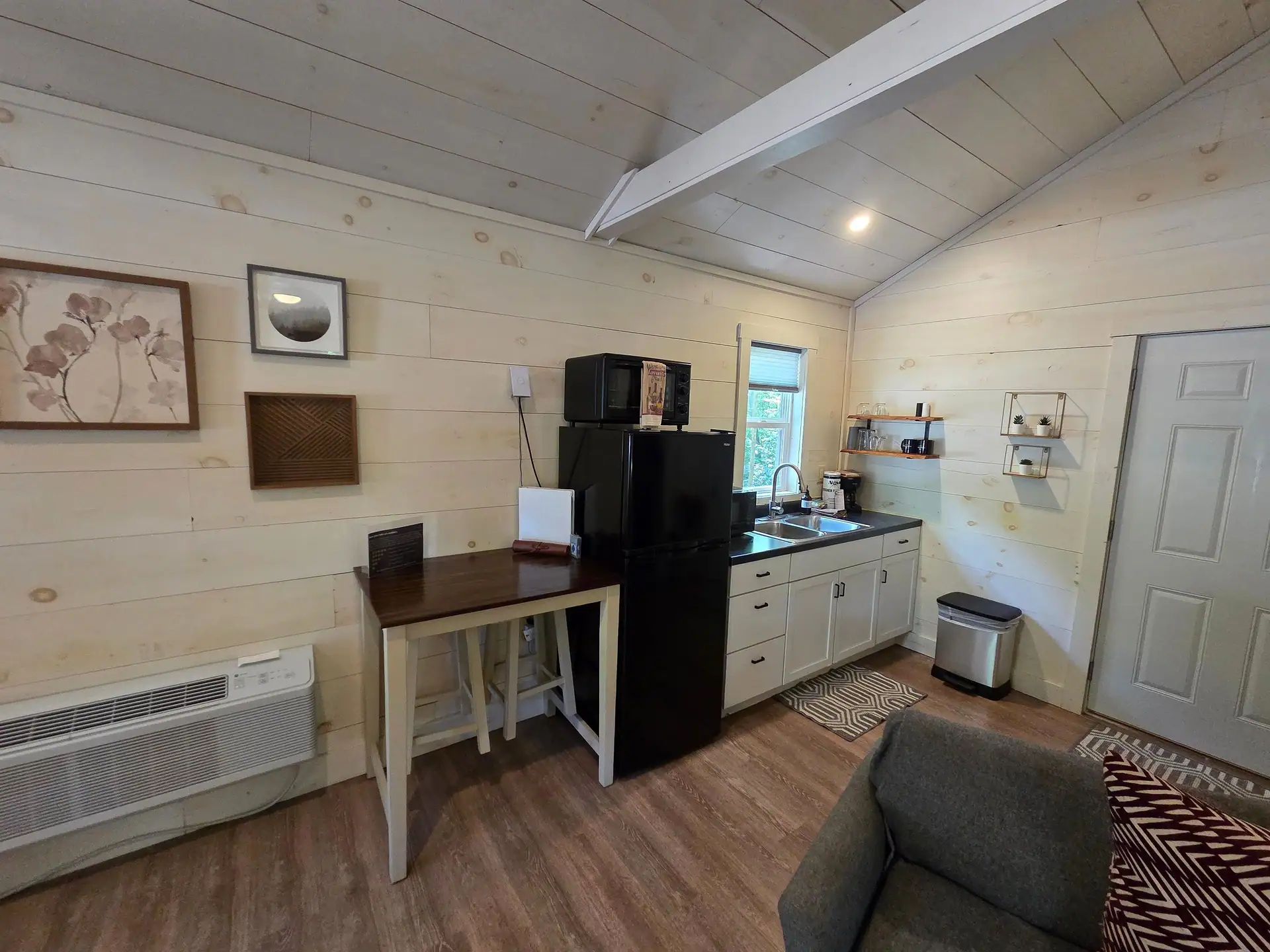 Kitchenette with white cabinets, black fridge, microwave, and wood dining table at Owl's Tale cabin