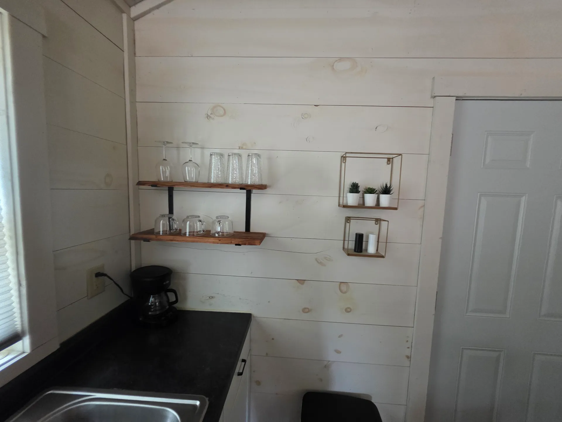 Open shelving with wine glasses, coffee maker, and small plants on shiplap wall at Owl's Tale cabin