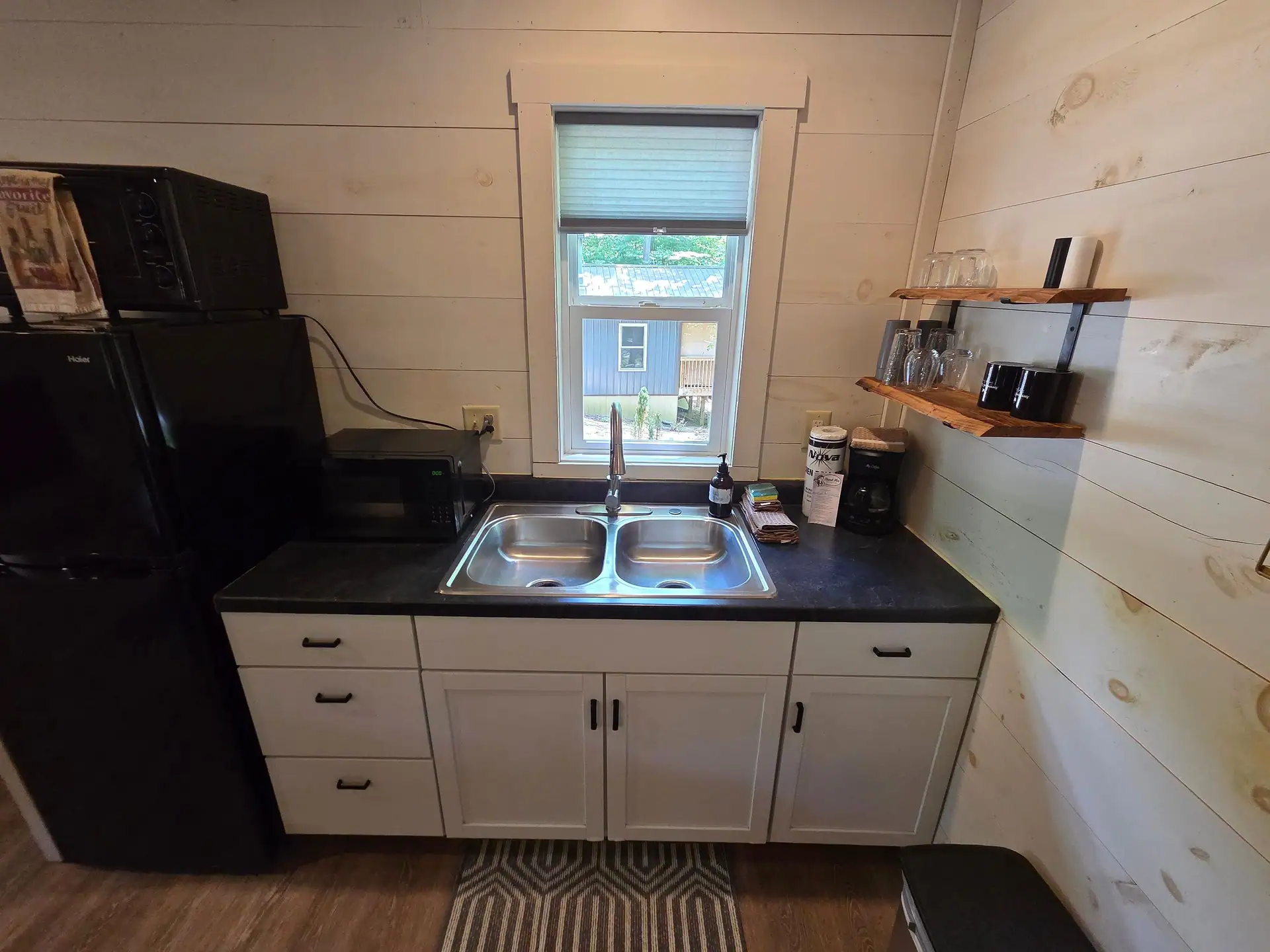 Kitchenette double sink under a window with open shelving for glasses and mugs at Owl's Tale cabin