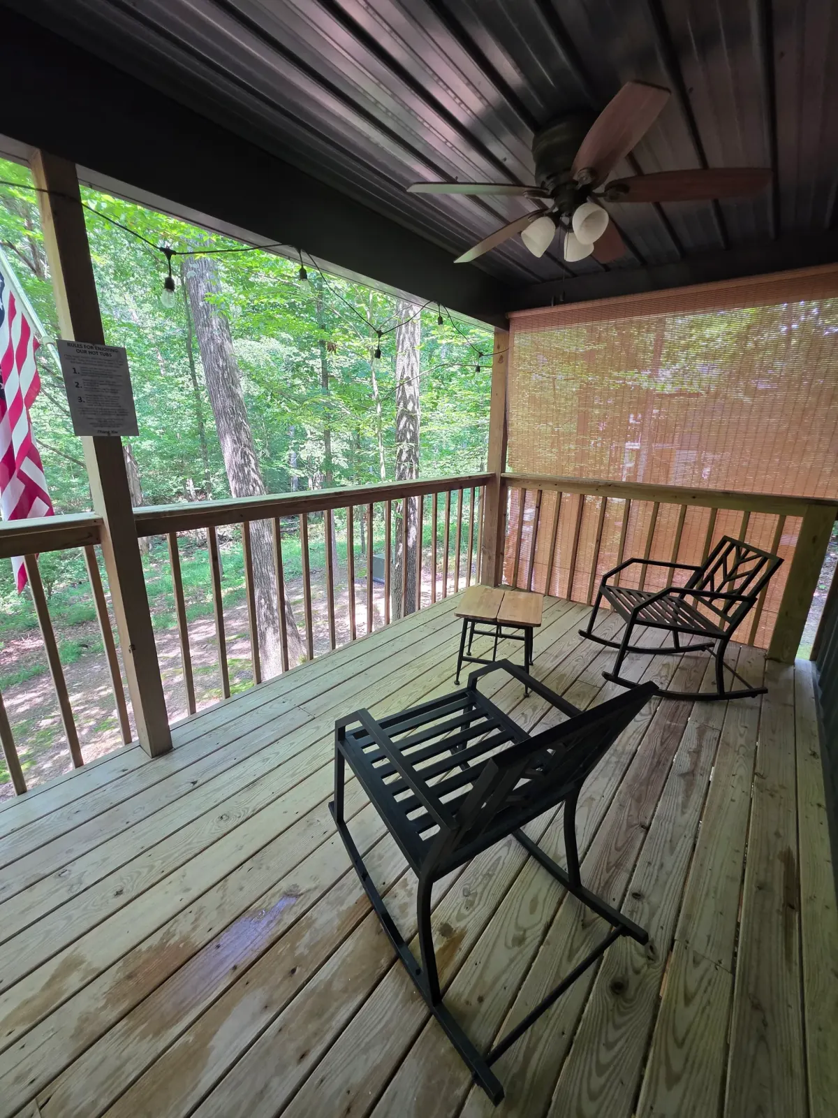 Covered front porch with black rocking chair and ceiling fan overlooking the forest at Owl's Tale cabin