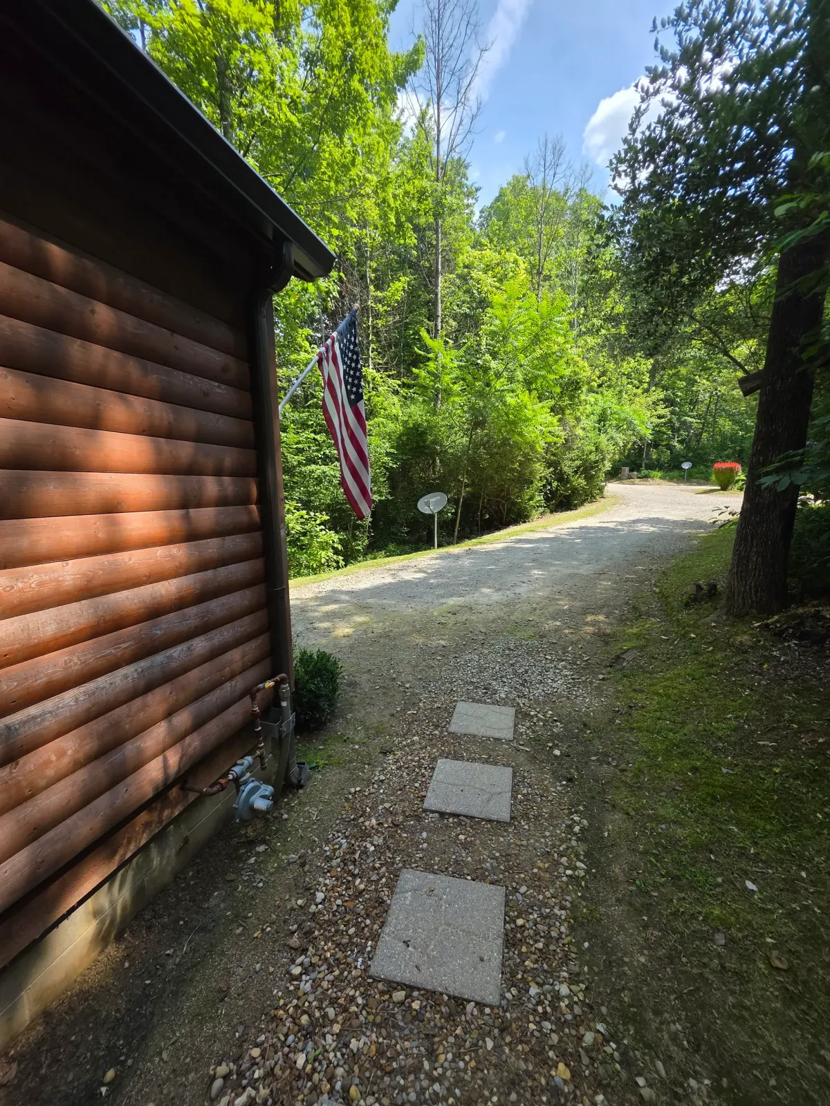 Settlers Roost cabin front view with gravel parking area, American flag, and stone stepping path