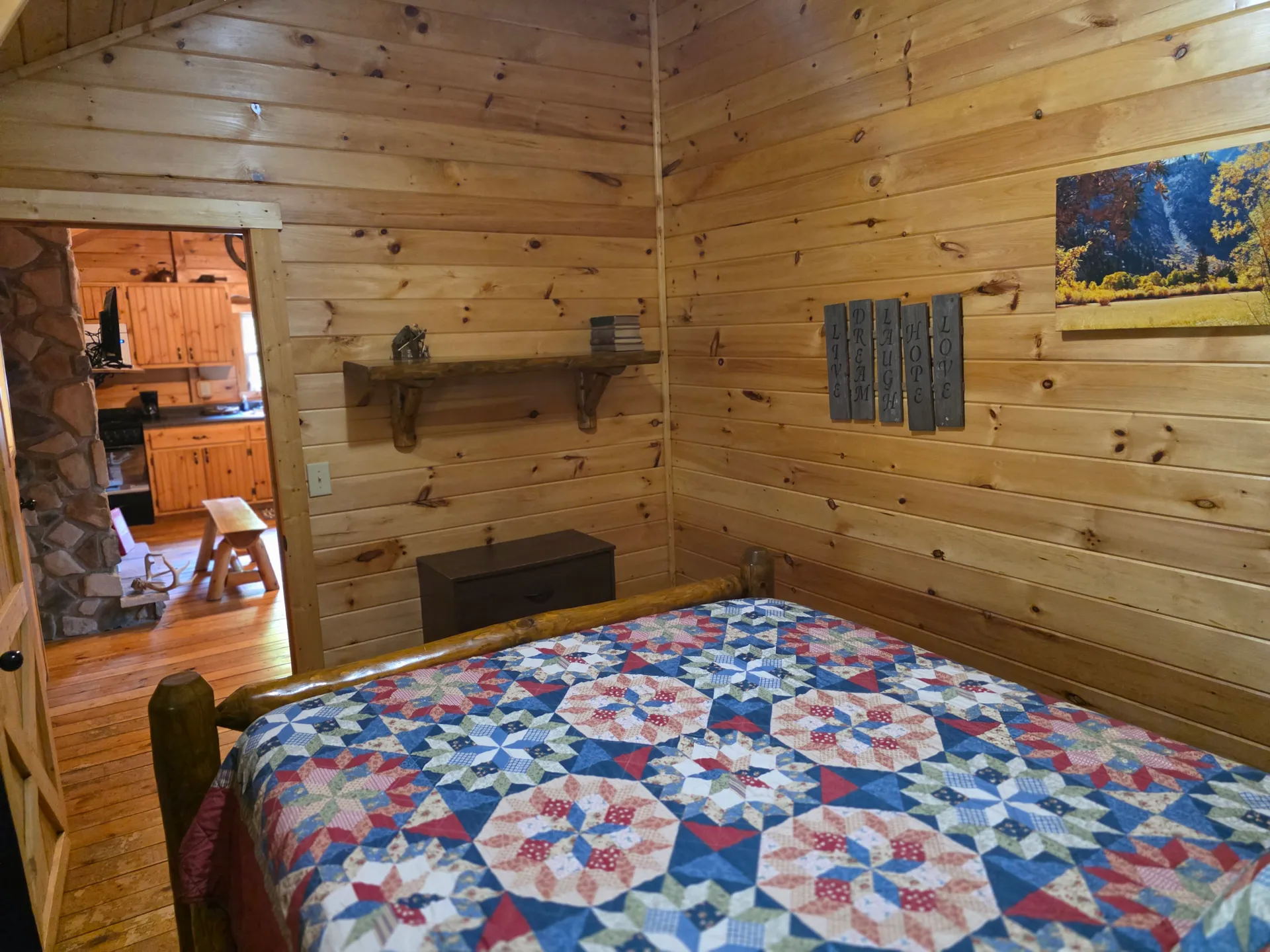 Queen bedroom with colorful patchwork quilt, rustic wall shelf, and nature artwork in Settlers Roost cabin