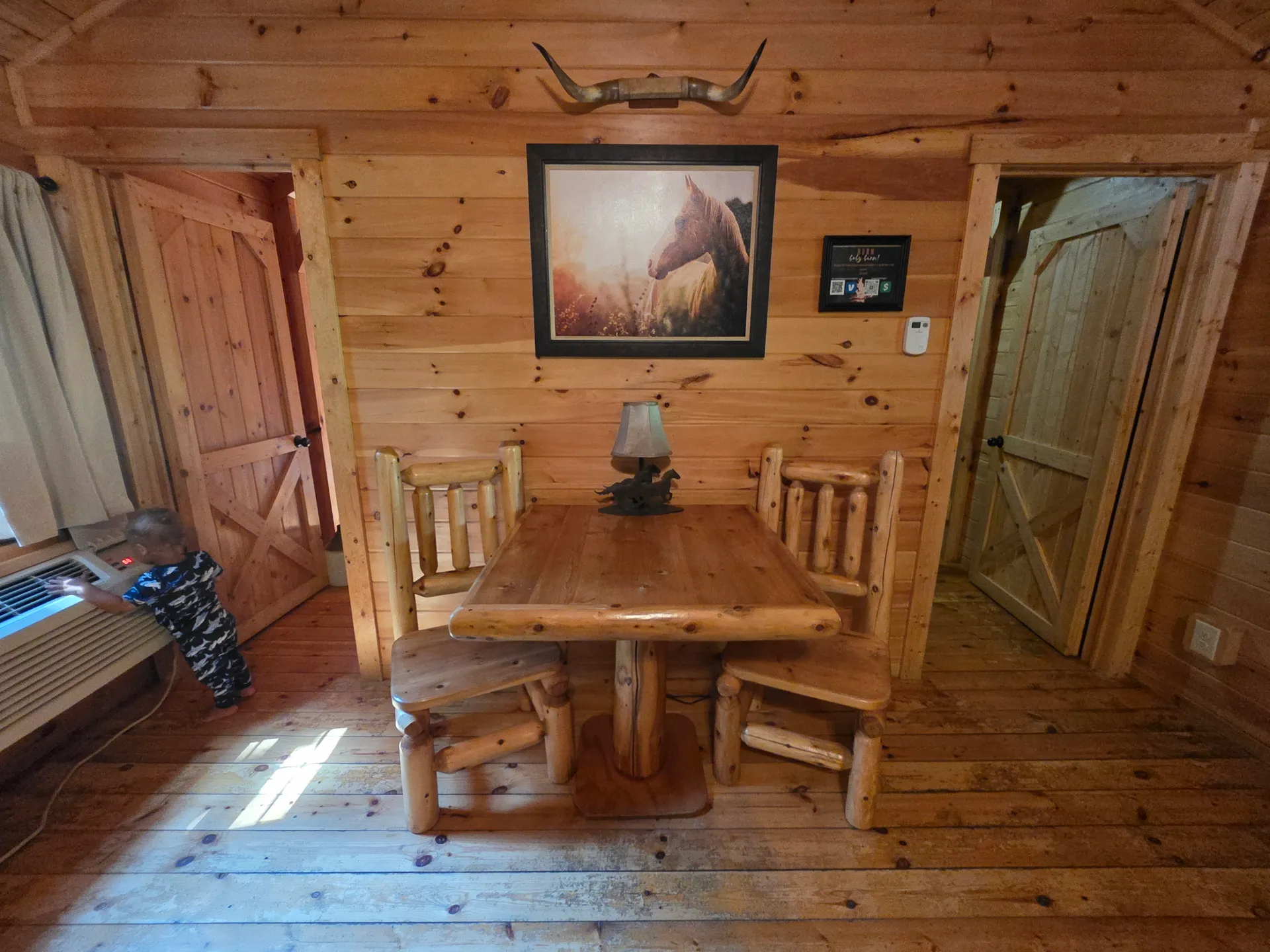Rustic log dining table with horse painting, antler mount, and barn-style doors inside Settlers Roost cabin