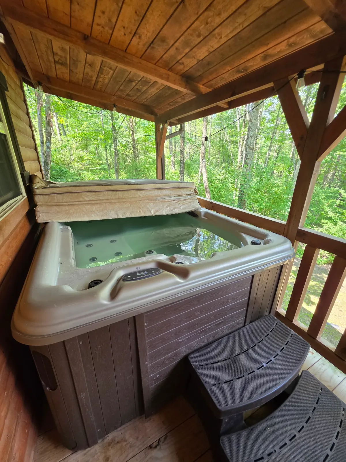 Private hot tub on the covered back deck of Settlers Roost cabin surrounded by Hocking Hills forest