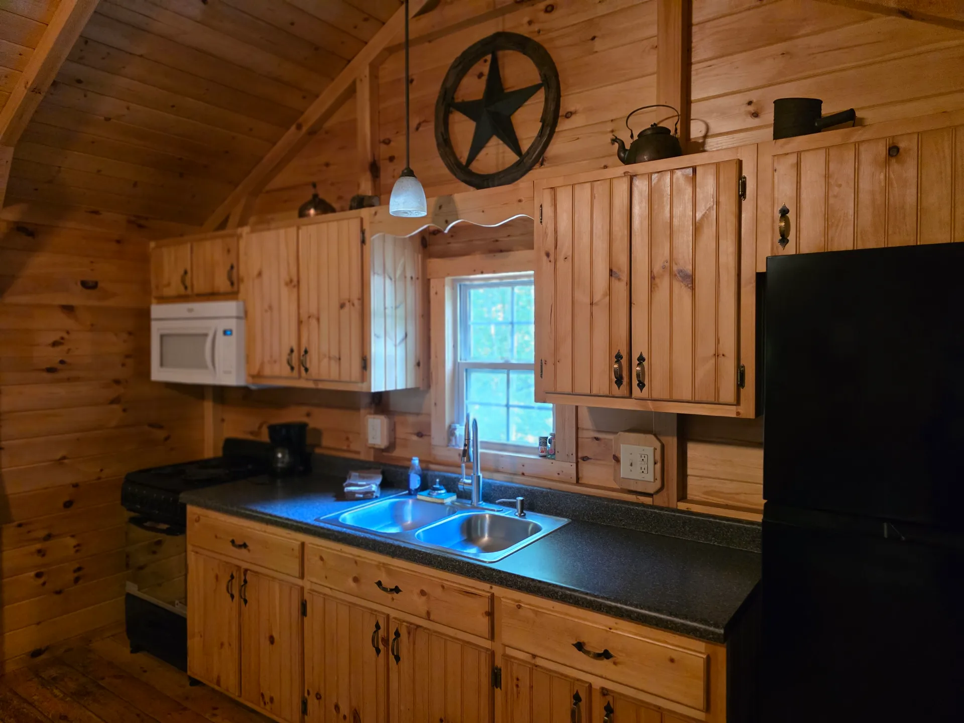Fully equipped kitchen in Settlers Roost cabin with pine cabinets, star wall decor, black appliances, and granite countertops