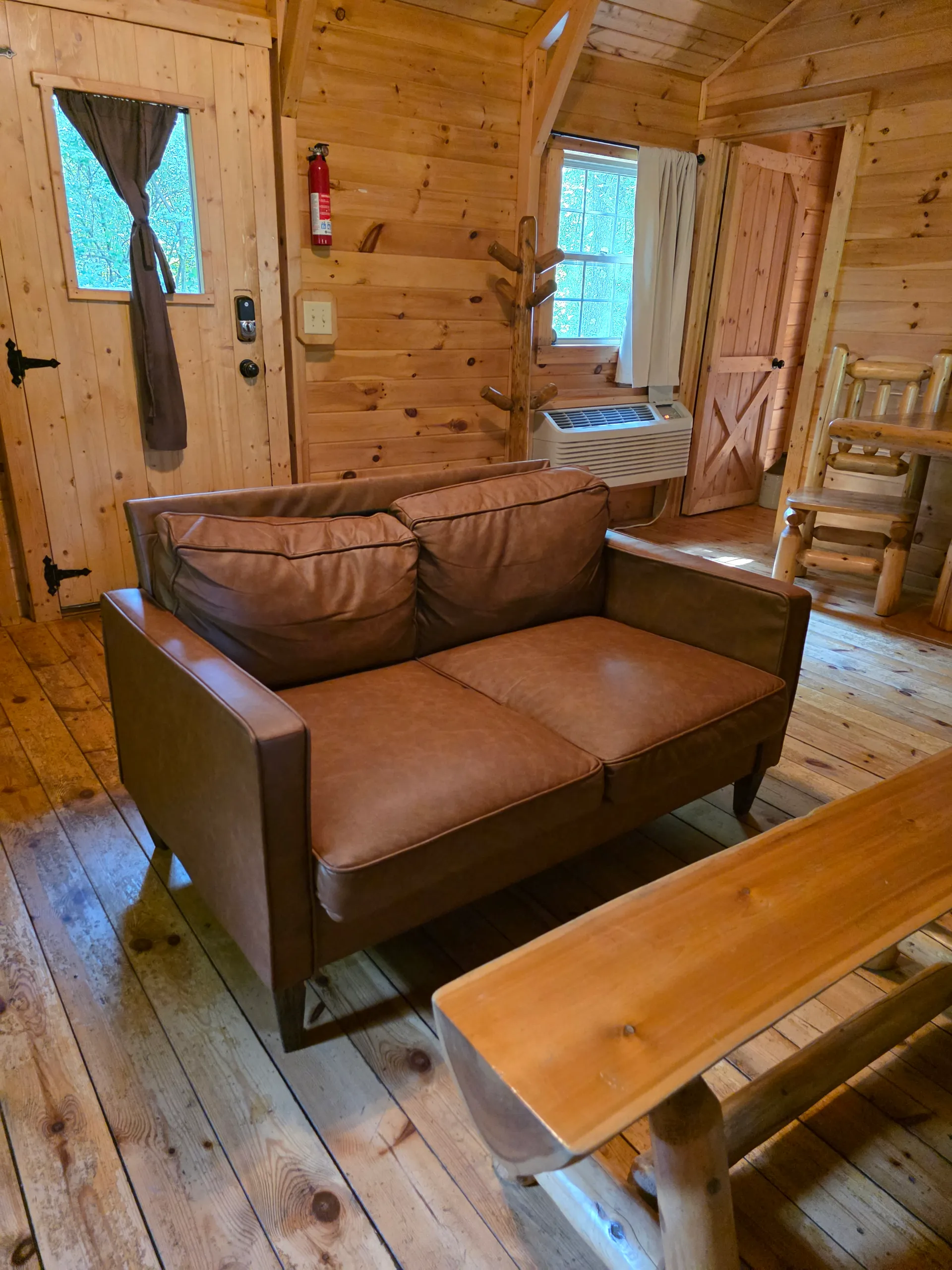 Leather loveseat and rustic log coffee table in the pine-walled living room of Settlers Roost cabin