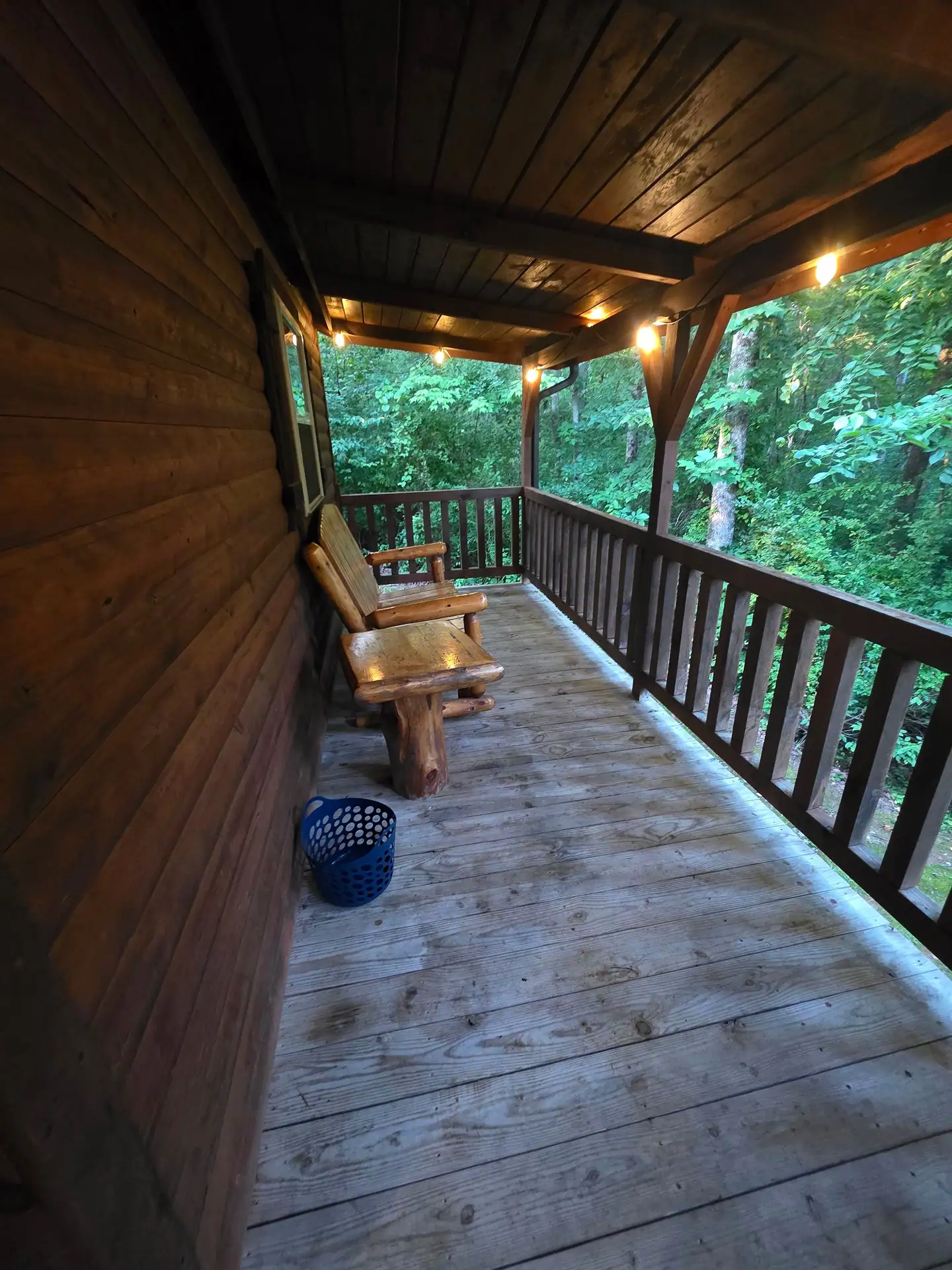 Covered back deck with a log bench and string lights at Whippoorwill