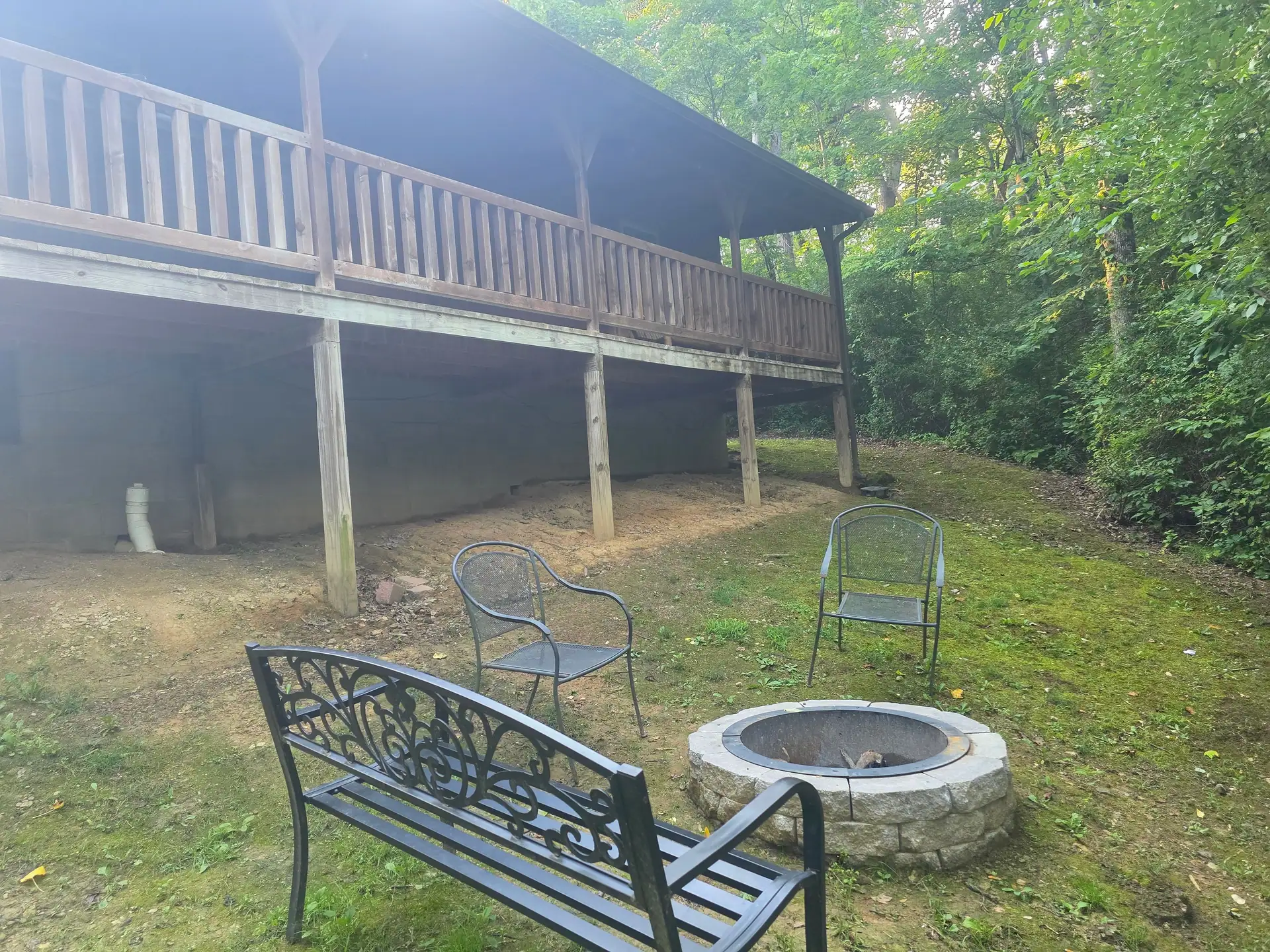 Stone fire pit with a bench and chairs behind Whippoorwill cabin