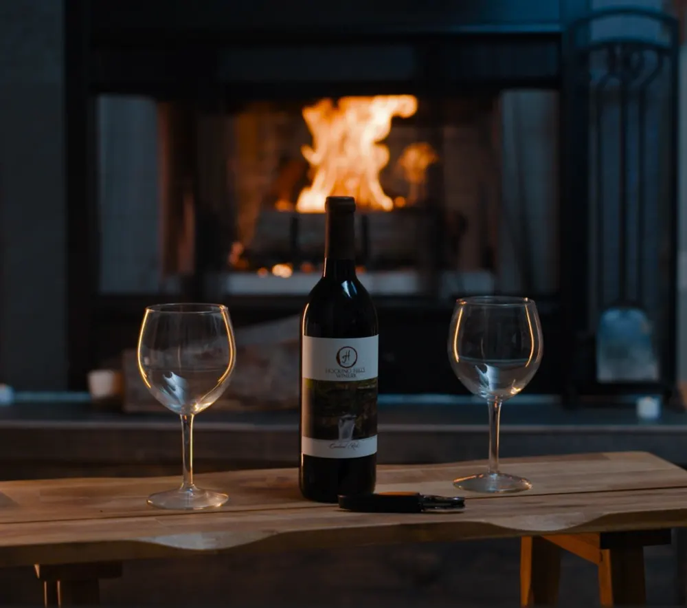 A bottle of local wine with two glasses by the fire